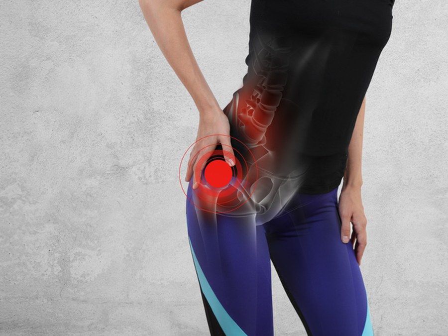 Hip and pelvis overlaid on a person holding their hip, with the painful joint marked